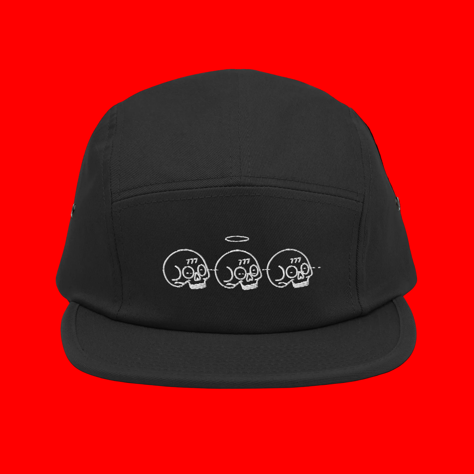 A black five-panel camp cap with a white embroidered graphic of three skulls and a halo on the front, displayed against a solid white background.