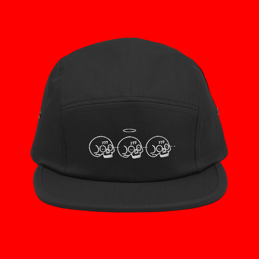 A black five-panel camp cap with a white embroidered graphic of three skulls and a halo on the front, displayed against a solid white background.
