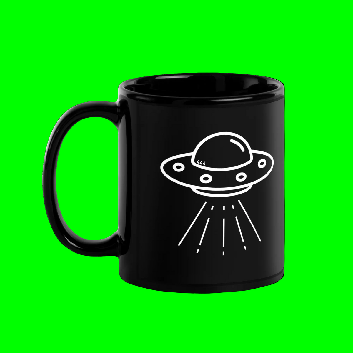 A glossy black ceramic mug with a white line-art graphic of a flying saucer UFO on the side, shown against a plain green background.